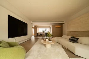 Comfortable living space with a couch, chair, dining table, and potted plants, lit by natural and artificial light
