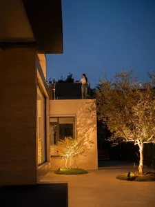 在夜晚，一個女人站在一座現代屋頂陽台旁，周圍的城市燈光和路燈點亮，創造出溫暖且吸引人的氛圍