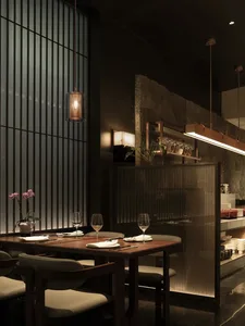 A dimly lit restaurant dining area with a table, chairs, and counter, featuring a combination of wood and metal elements, wine glasses, and decorative items