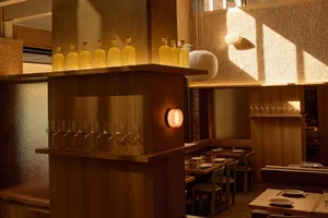 Cozy modern restaurant with a wooden bar, tables, and chairs, dim lighting, and wine glasses on tables