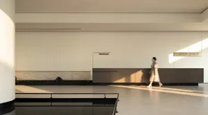 A modern lobby with a white wall, a bench, a chair, and a handbag, lit by natural light from windows