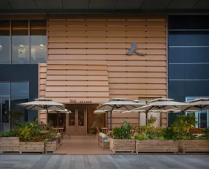 Photograph of a restaurant exterior with a wooden facade, umbrellas, chairs, and dining tables, creating a cozy outdoor seating area