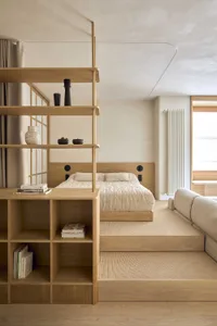 Cozy bedroom with a bed, bookshelf, and couch, featuring wood furniture and a neutral color palette