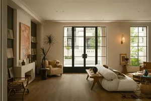 Cozy living room with a couch, chair, and dining table, featuring a potted plant, vase, and bowl, with natural light streaming in through a large window
