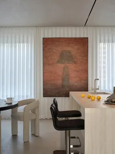 A modern kitchen and dining area with a marble countertop, white walls, a black chair, and a large painting on the wall, set in a warm and inviting dimly lit space