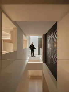A man stands in a modern room with a white wall, glass wall, and black and white color scheme, creating a calm and serene atmosphere