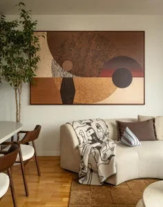 A modern living room with a couch, chair, and dining table, featuring a large painting on the wall and a comfortable, inviting atmosphere