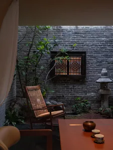 Cozy living room with a brick wall, stone floor, a chair, a dining table, and a potted plant, lit with dim lighting