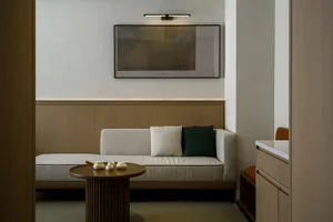 Cozy living room with a white couch, a brown chair, a wooden floor, and a painting on the wall, lit by dim lighting