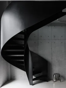 A black and white photo of a spiral metal staircase in a dimly lit room with a metal trash can at the base
