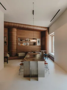 A well-lit living room with a modern design, wooden elements, and a large window, featuring a dining table and chairs, a couch, and a comfortable atmosphere