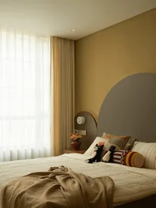 Cozy bedroom with a bed, mirror, and window, featuring a yellow wall, a blanket, pillows, and stuffed animals