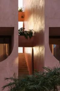 Photograph of a pink building with a concrete staircase and metal railing, set against a white background, with natural sunlight creating a warm atmosphere