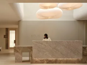 A modern lobby with a white marble countertop, grey marble wall, and a woman standing in front of the counter, with a nearby bench in a soft and inviting atmosphere