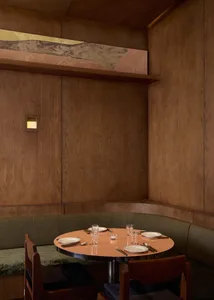 A dimly lit dining room with a wooden table and chairs, surrounded by plates, cups, and utensils, set against a brown color scheme