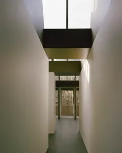 Narrow hallway with a vaulted ceiling, white walls, and natural light from unknown sources