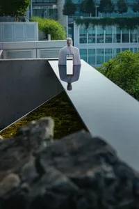 A stone sculpture of a man sitting on a bench in an outdoor area with a building in the background, surrounded by a calm and contemplative atmosphere