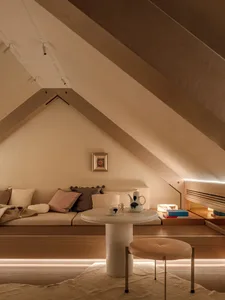Cozy modern living space with a wooden floor, a couch, chair, and dining table, with books and a cup scattered around, dim lighting creating an intimate atmosphere