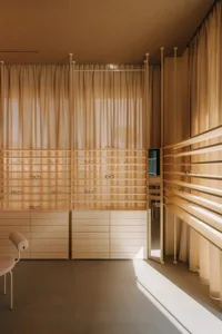 A bright and organized storage space with a wooden floor, white walls, and natural light from the windows, featuring shelves, drawers, and a chair and couch