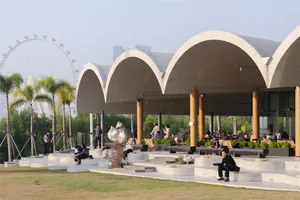 A large modern building with a high ceiling and open space filled with people, dining tables, and chairs, featuring a predominantly white color scheme and soft warm lighting