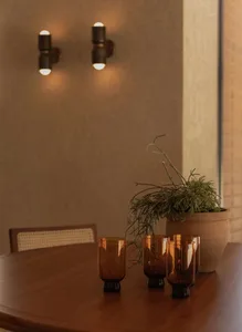 A modern living room with a wooden dining table, four candles in glass vases, and a potted plant, surrounded by clean lines and minimalistic decor