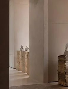 A cozy living space with a white wall, a bookshelf filled with books of various sizes and colors, and three vases in different materials placed at different heights on the shelf