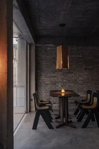 Cozy dining area with a brown table, black chairs, and a brick wall, dimly lit for an intimate atmosphere
