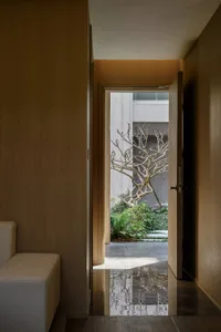 Cozy living room with a wooden floor, a wooden door, and a view of the patio through an open doorway, featuring a tree and a warm atmosphere