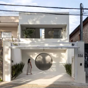 A modern white house with a circular window on the front, surrounded by a well-maintained garden