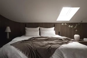 Cozy bedroom with a bed, a window, and a potted plant, featuring a blanket, pillows, and natural light