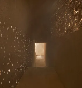 A simple functional hallway with concrete walls, lights on the wall, and a doorway leading to another room, creating a warm and inviting atmosphere