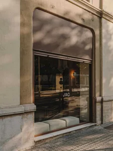 A serene outdoor scene of a building's exterior with a large window featuring a reflection of a bench and chair, set against a concrete backdrop