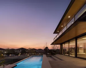 A modern house with a wooden facade, a blue pool, and a deck, set against a warm sunset backdrop