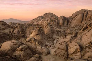 A desert landscape with a rocky hillside and mountain in the background, featuring a mix of light and dark rock formations