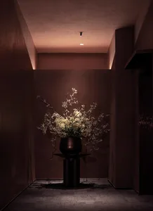 A small, dimly lit room with a brown color scheme, featuring a vase with flowers on a table as the main focus
