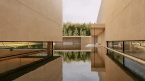 A modern lobby with a reflecting pool surrounded by a concrete structure, glass, and wood, featuring a bench and soft, diffused lighting