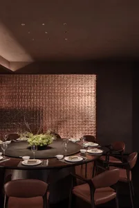 Cozy modern dining space with a round table, chairs, and a potted plant, set with plates, wine glasses, and utensils