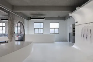 A modern kitchen with a white countertop, sink, and refrigerator, flooded with natural light from the windows, creating a calm and inviting atmosphere