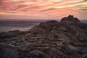 A group of stone houses built into a rocky mountain, set against a pink sky