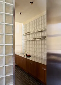 A modern kitchen with a wooden cabinet and glass door, featuring a vase with flowers and wine glasses on the counter, in a well-lit space with a warm atmosphere
