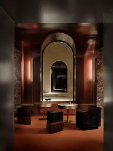 A modern living dining area with a brown color scheme, featuring a large arched doorway, a mirror, and a table with chairs, surrounded by a well-lit space with natural light