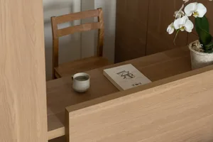 A cozy home office with a wooden desk, chair, and vase with flowers, lit by natural light