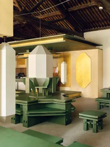 Cozy modern restaurant with a wooden floor, gold walls, and dim lighting, featuring a dining table, chairs, vases, and lamps