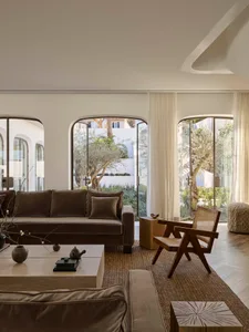 A warm and inviting living room with a brown couch, chair, and coffee table on a wooden floor, decorated with vases, bowls, and a potted plant, with natural light and comfortable furniture arrangement