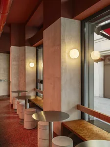 A modern restaurant interior with a row of wooden tables and metal chairs, illuminated by natural light through windows, creating a warm and inviting atmosphere