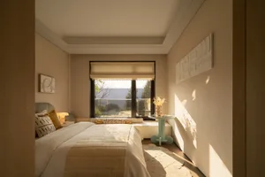A well-lit bedroom with a modern style, featuring a white comforter, a table, and a potted plant, with a cozy and inviting atmosphere