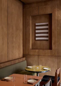 A modern dining room with a wooden table and chairs, set with plates, glasses, and utensils, surrounded by wooden walls and soft, diffused lighting