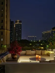 A spacious living room with a glass balcony, furnished with a couch, dining table, and potted plant, illuminated by natural light and featuring a modern and stylish aesthetic