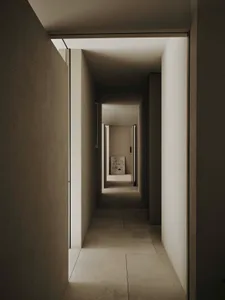 Narrow hallway with a stone floor, a chair, and a cat, in a dimly lit space with a white color scheme