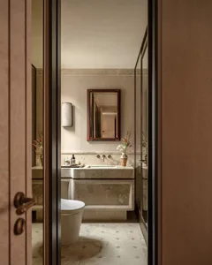 A dimly lit bathroom with a white toilet, sink, and bathtub, set against a residential background with a brown door
